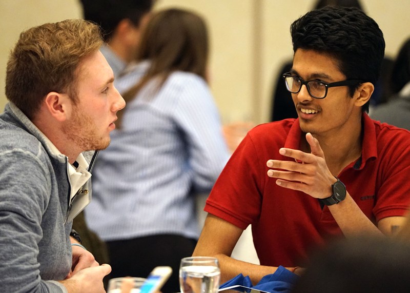 Nisarg Jhaveri speaks with another young man at a table.