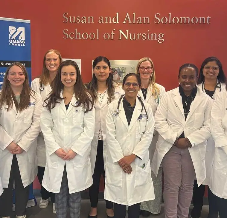 Nursing students stand before the Susan and Alan Solomont School of Nursing wall at UMass Lowell.