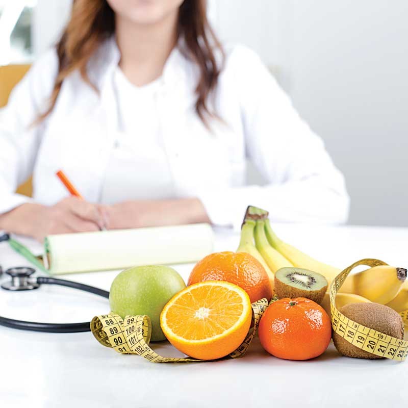 Assorted fruit with a measuring tape, stethoscope, and person taking notes in the background