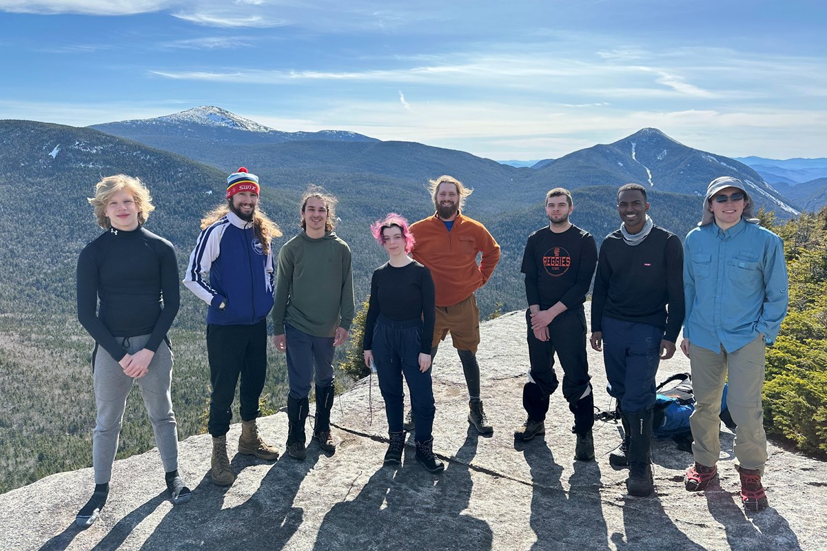 Eight people pose for a photo while standing on a mountain top.