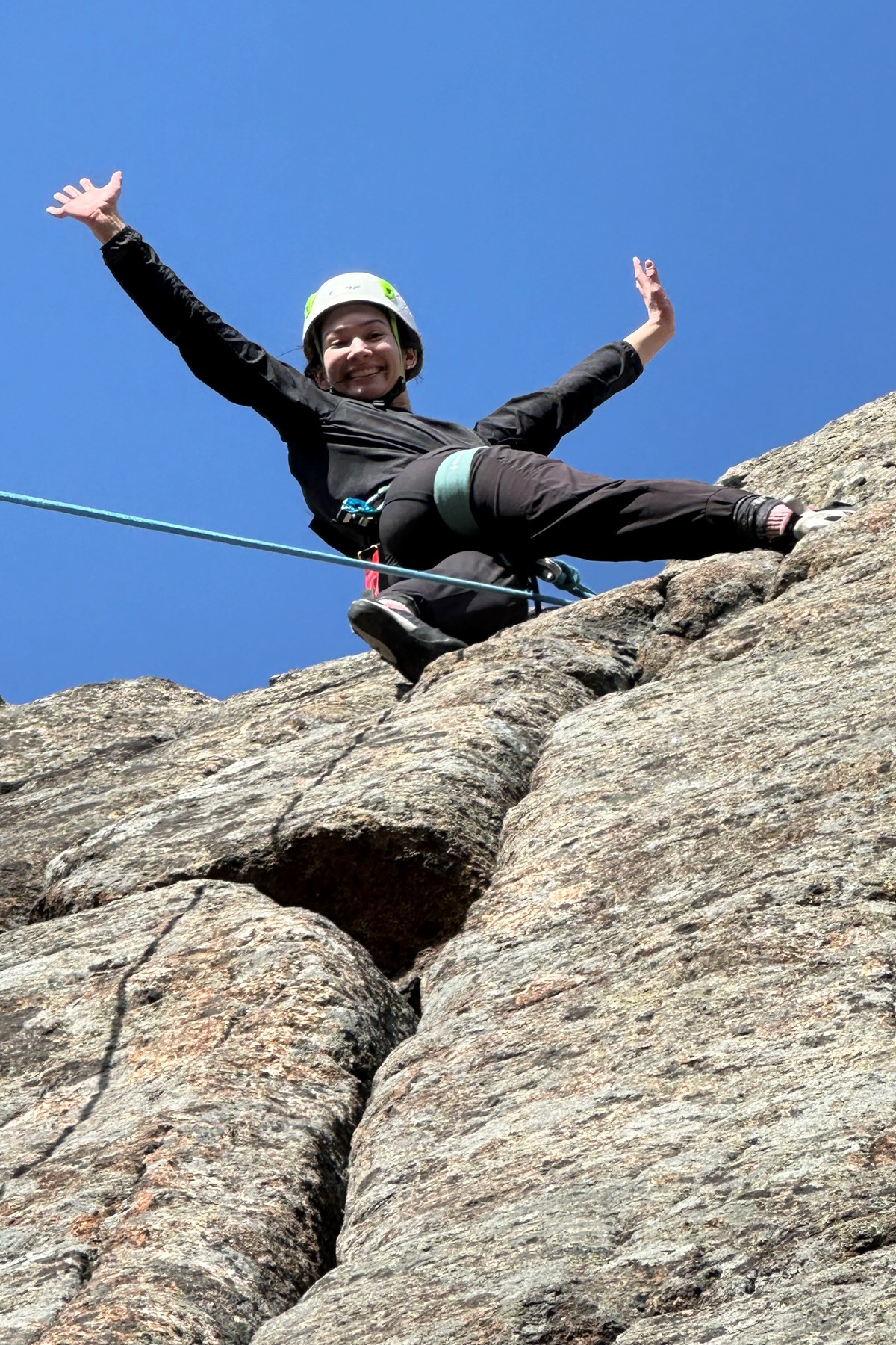 A person spreads their arms and poses for a photo while rock climbing.