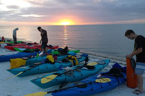 Students beach their kayaks as the sun sets