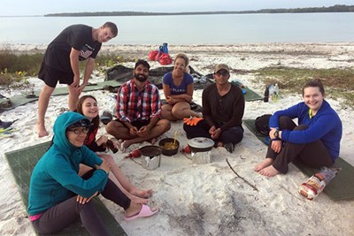 Students enjoy dinner while camping on the beach