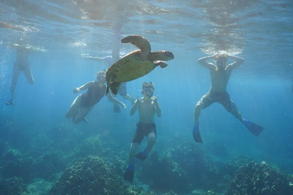 Ten people pose for a group photo while sitting on a boat with the sun setting behind them.