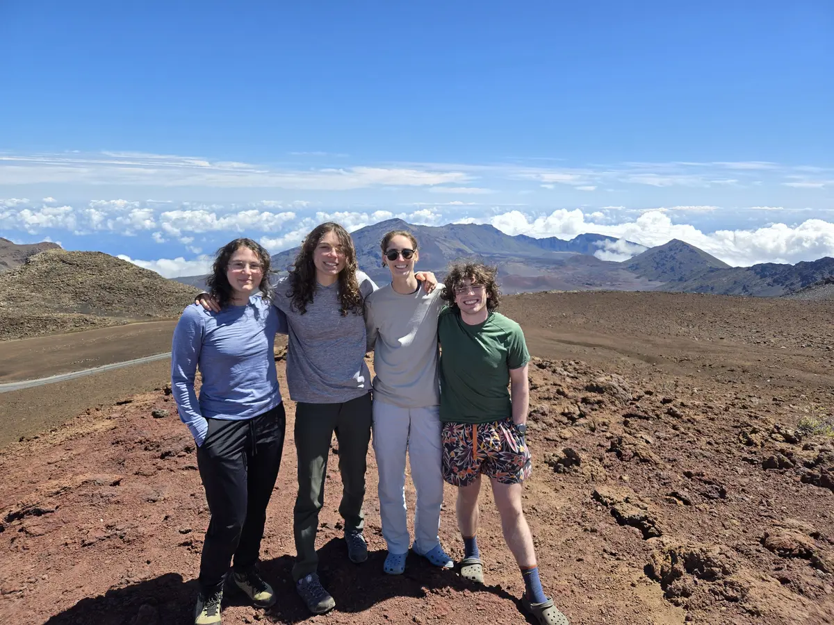 Four people pose for a photo while standing in front of cloud-topped mountains.