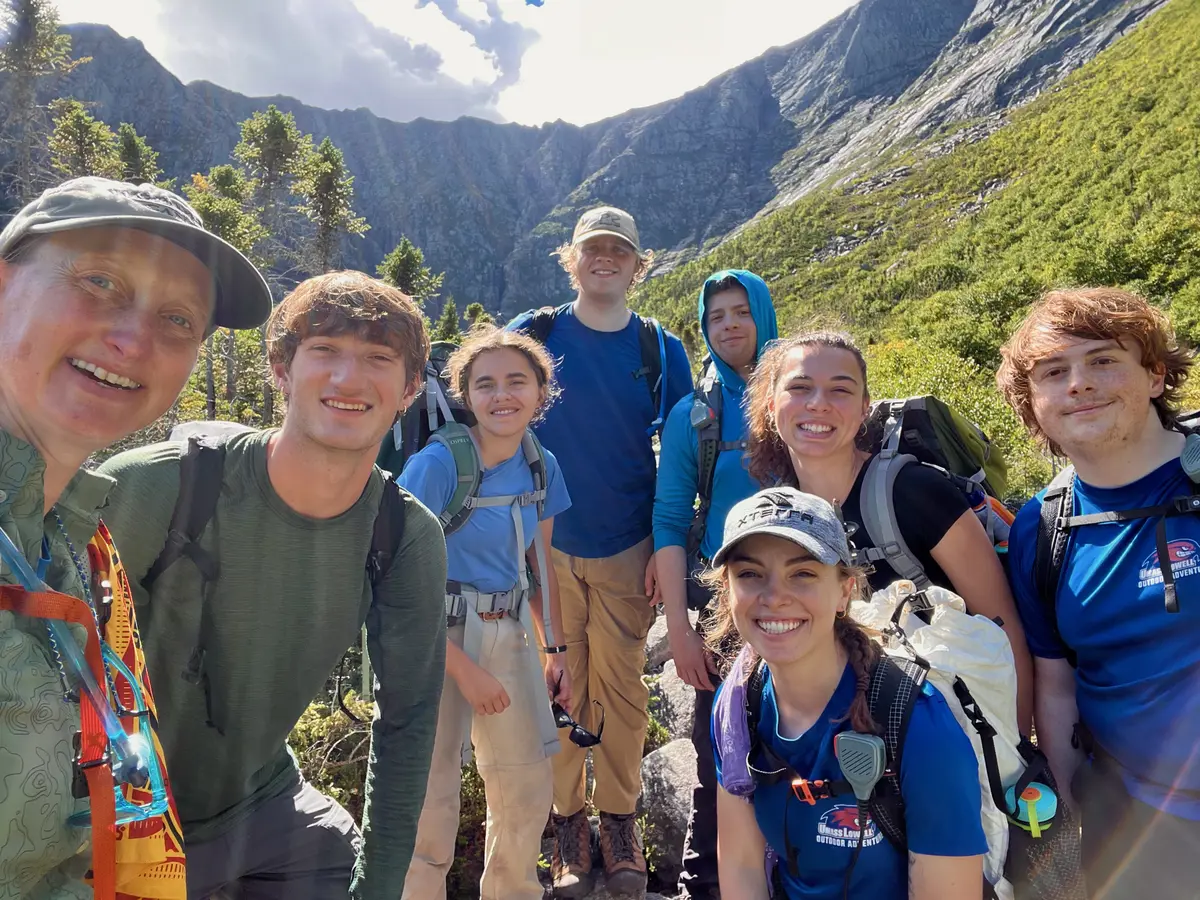 Eight men and women pose for a group selfie photo while hiking a mountain.
