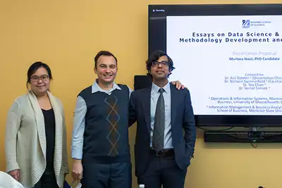 A woman and two men pose for a photo in front of a TV monitor