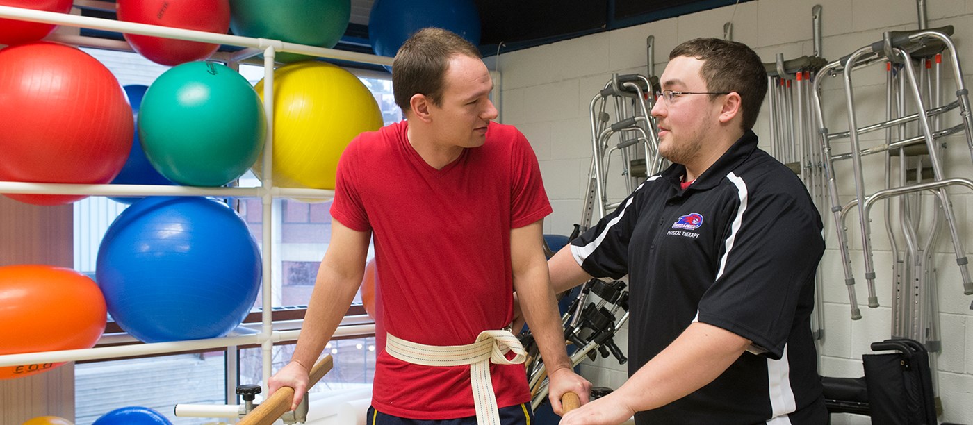 Physical therapy student helps patient walk using bars
