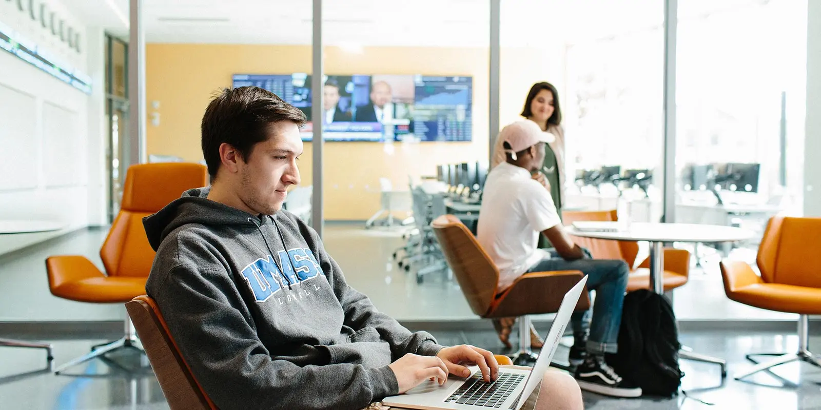 Male student on laptop in foreground in the lobby of Pulichino Tong Business Center