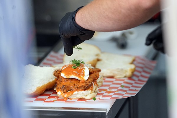 A man wearing black gloves sprinkles herbs on top of a chicken parm sandwich