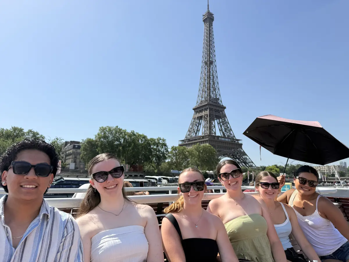 Students on open top tour bus holding sun umbrella Eiffel Tower in background