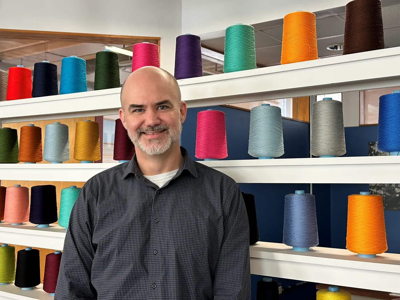 Paul Kuttner stands in front of large spools of colorful cotton thread for weaving
