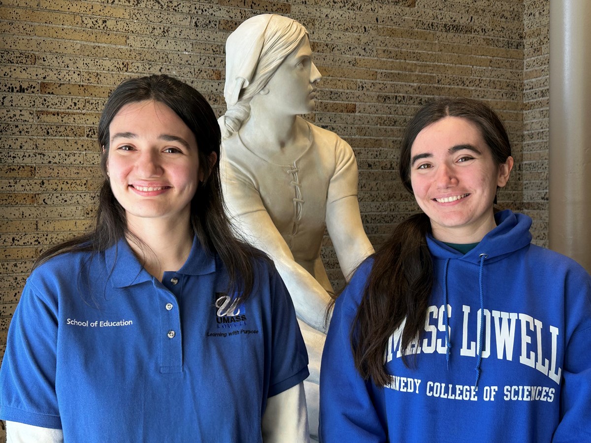 Eleanora Peters, wearing a UML School of Education shirt, and Regina Peters, wearing a Kennedy College of Sciences sweatshirt, frame the statue of Joan of Arc in Coburn Hall