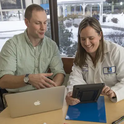 Two people look at a laptop and tablet together.