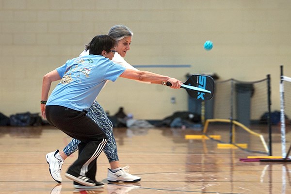Two women lunge to hit the ball while playing pickleball