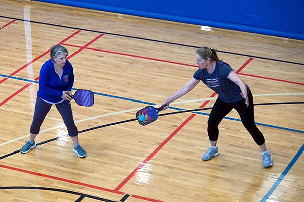 A woman hits the ball while her pickleball teammate looks on 