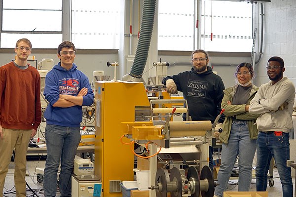 Plastics Engineering undergraduate and Ph.D. students stand in front of a revitalized extrusion machine.