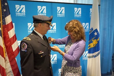 A woman in a purple sweater places a pin on the lapel of a man in a police uniform