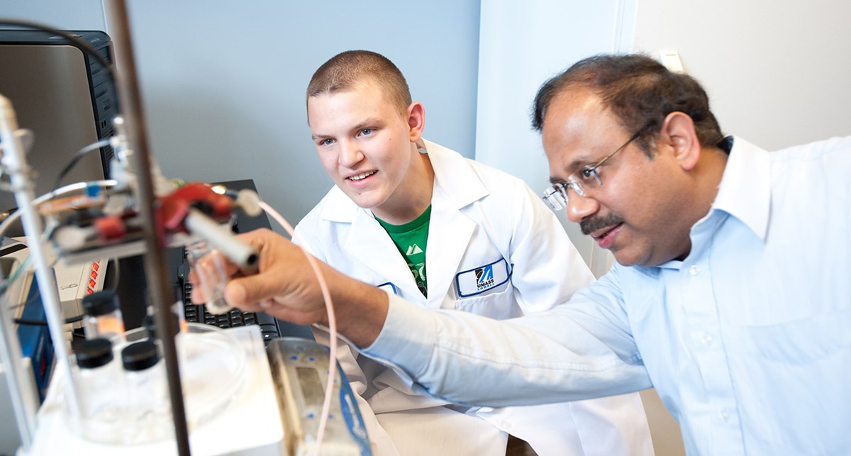 UMass Lowell Professor Pradeep Kurup working with  a male student in a lab coat.