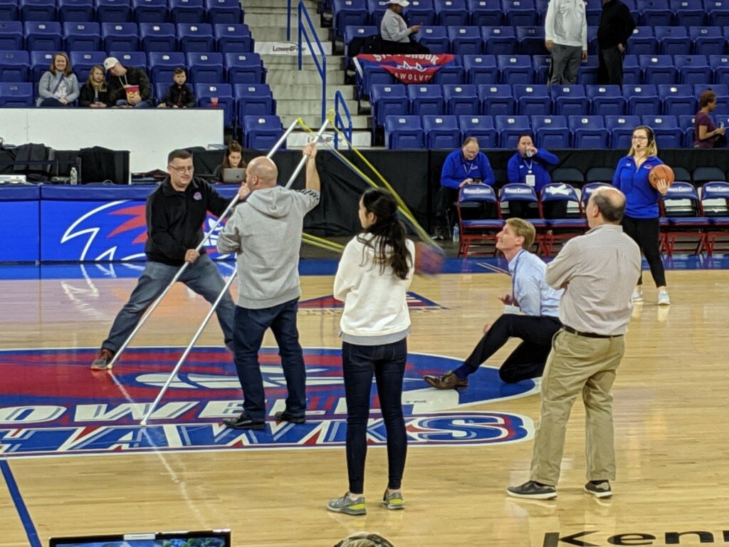 UMass Lowell Provost Joseph Hartman launches a basketball from half court using a slingshot during Basketball Week activities