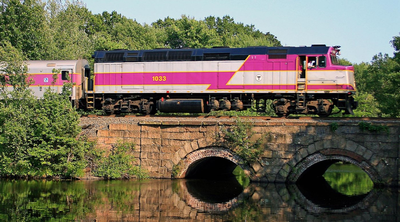 An MBTA commuter train travels on a bridge over a river.