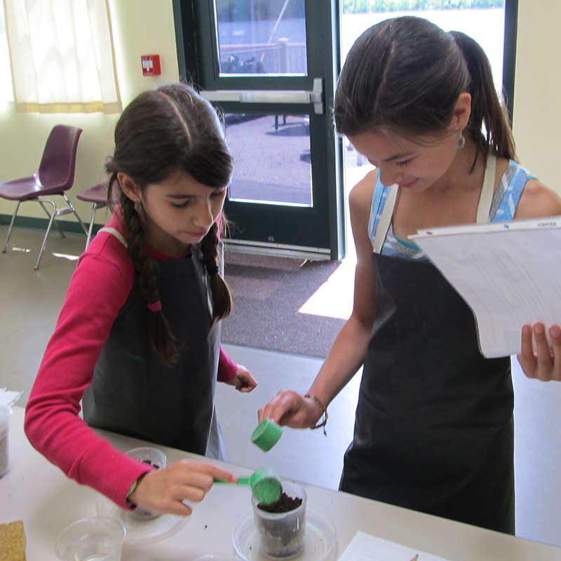 Two school-age girls filling cups with dirt at Tsongas Industrial History Center