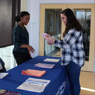 Two women discuss info standing across a table with piles of papers