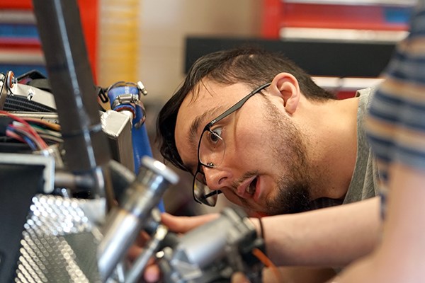 A student wearing glasses concentrates on work he is doing to a race car