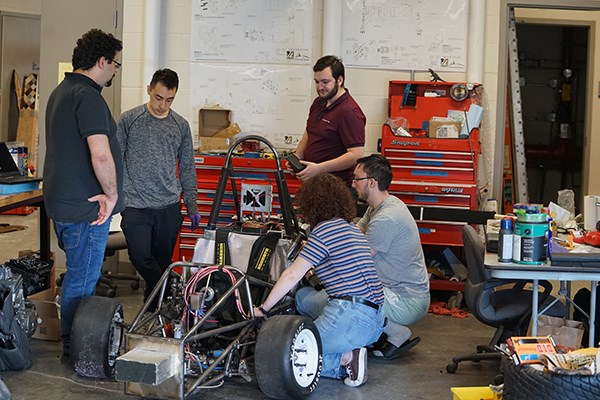 Five students work on a race car in a garage