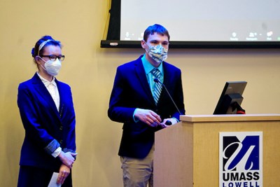 A student in a suit jacket and tie makes a presentation with another student who is wearing glasses