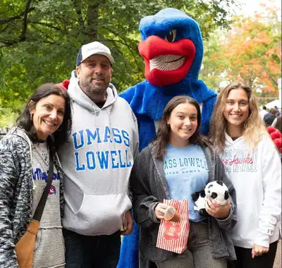 A family of four stands with Rowdy the River Hawk at Homecoming.