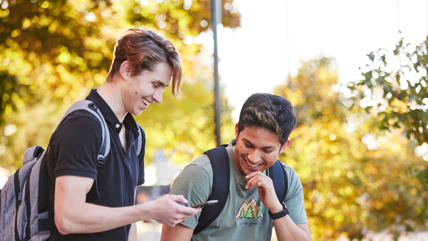 2 students looking at cell phone while walking