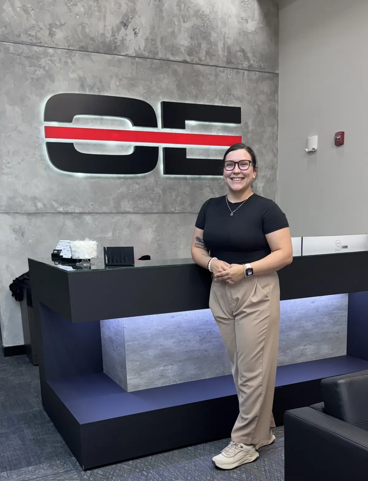 Rebecca Waupoose in front of a wall with Optiline Enterprises logo on it