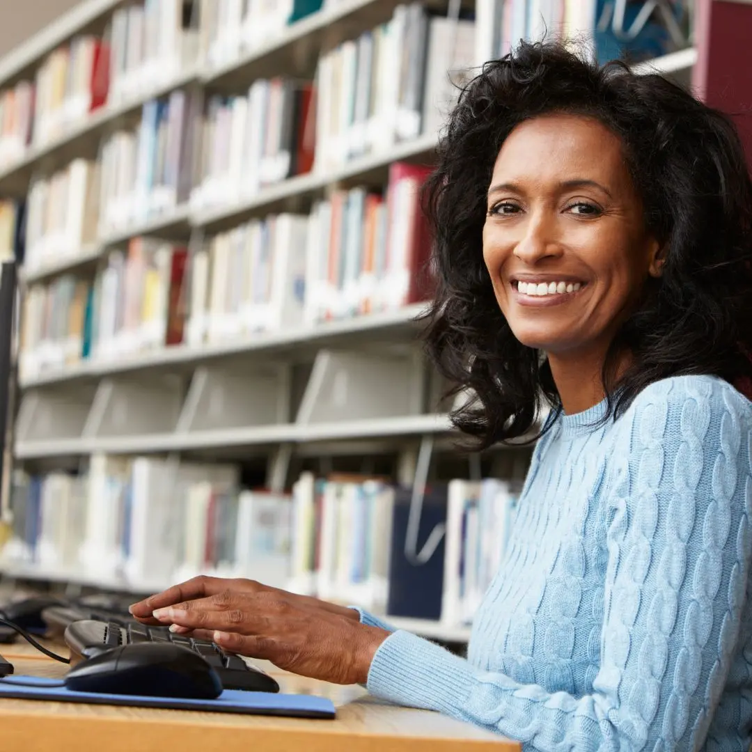 A person using a computer at a library looking at the camera.