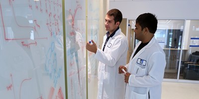 Researchers in lab coats writing formulas on a whiteboard
