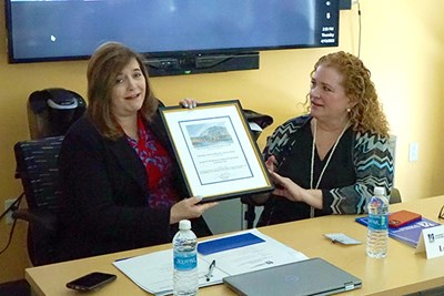 A woman reacts after being presented with a framed certificate by another woman
