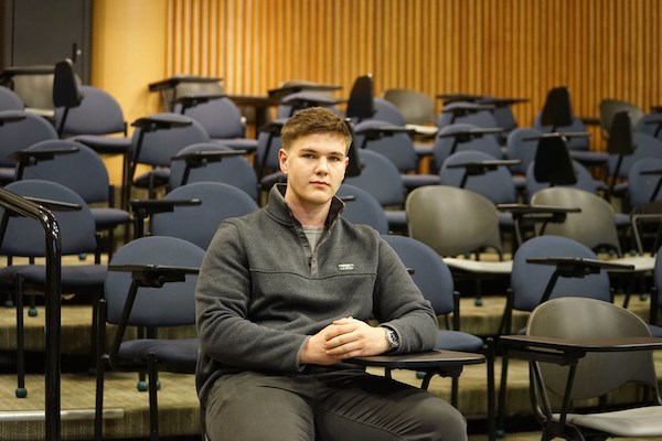 A male student sits at a desk in an empty auditorium  