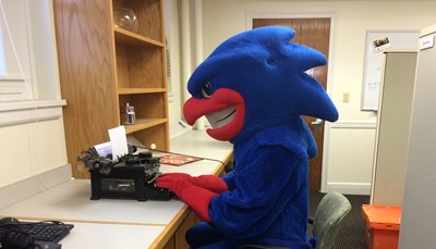  Rowdy the River Hawk (mascot) sitting typing at a typewriter.