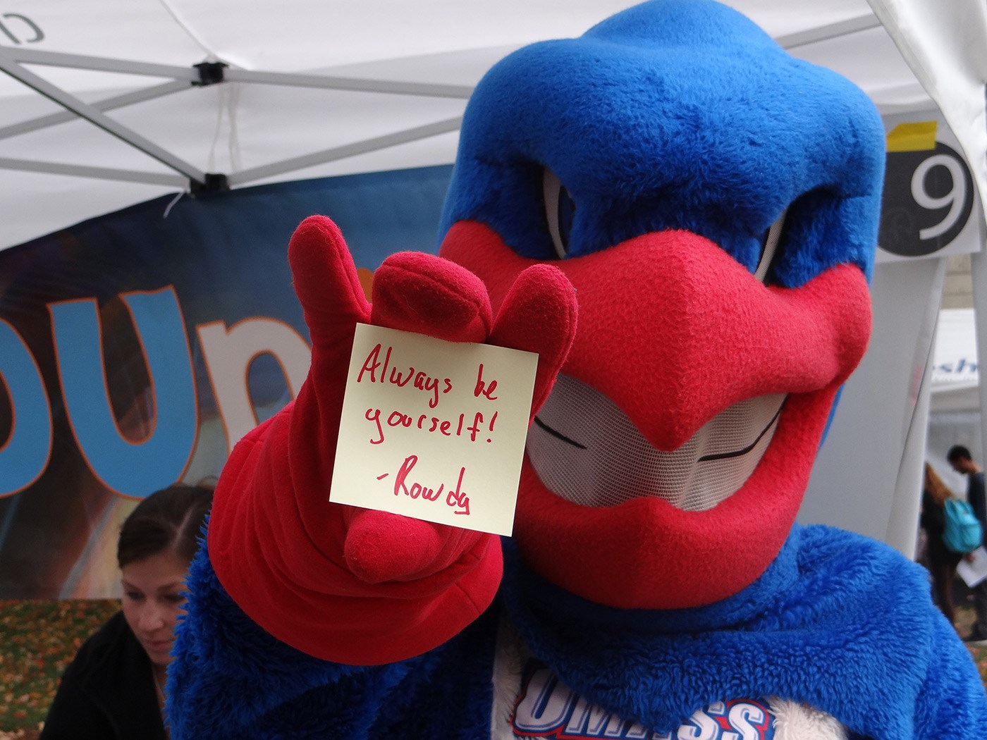 UMass Lowell mascot, Rowdy the River Hawk holding out a post-it note that say "Always be yourself!"