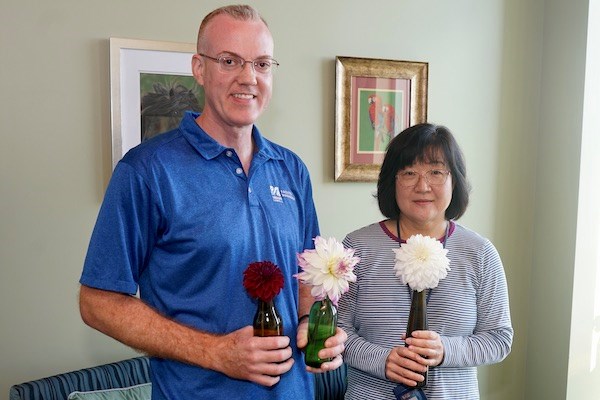 A man in a blue shirt poses for a photo with a woman as they both hold flowers