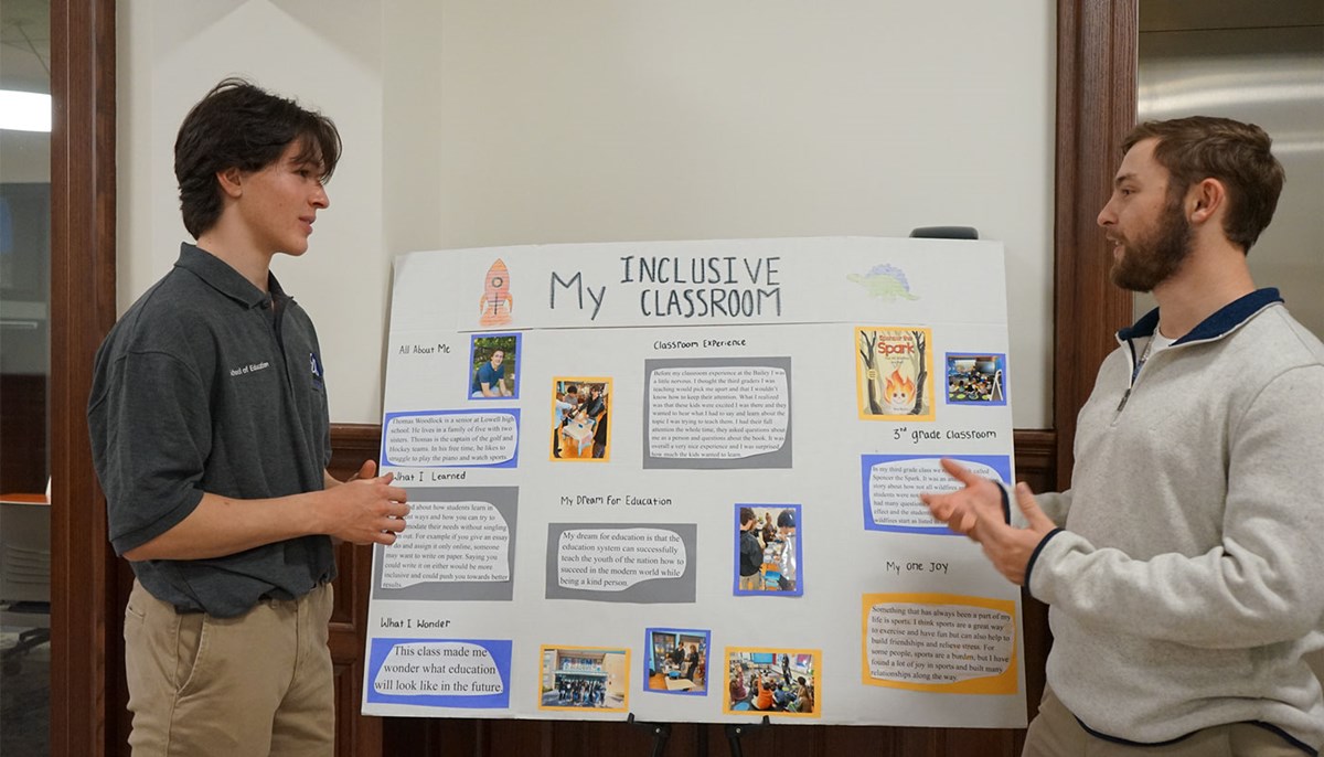 Ryan Descheneaux talks with another student in front of a project poster board.