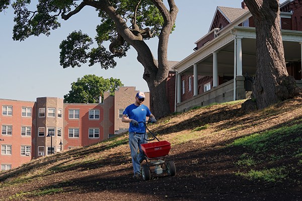 A grounds employee spreads seed behind the Allen House on South Campus
