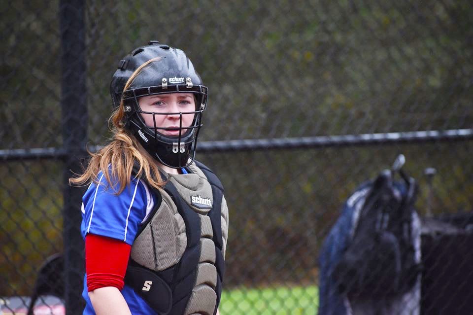 Softball catcher looks to the dugout with helmet on