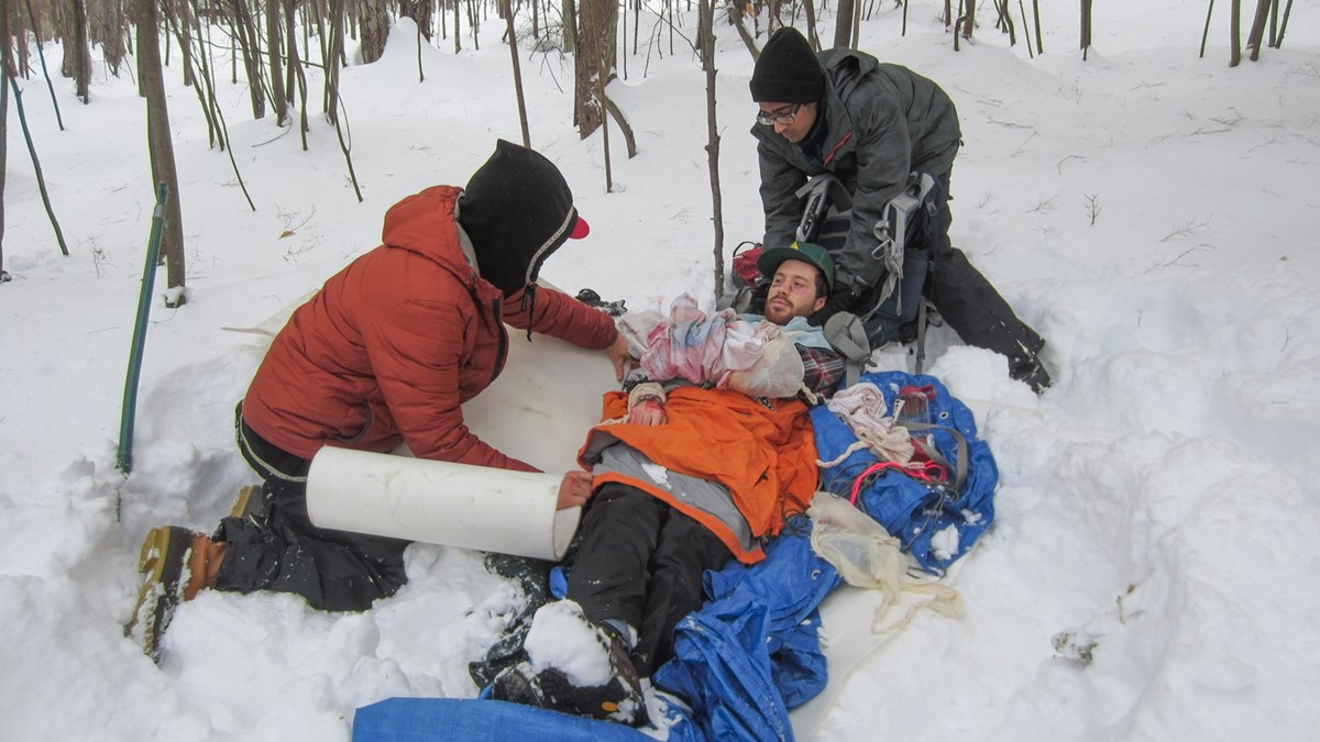 Picture of Wilderness Medicine class scenario with two people assisting an injured man in the snow laying on tarps