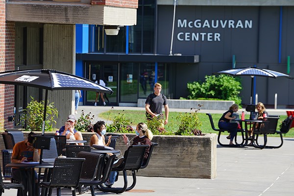 Students sit under solar umbrellas on campus as a student walks by