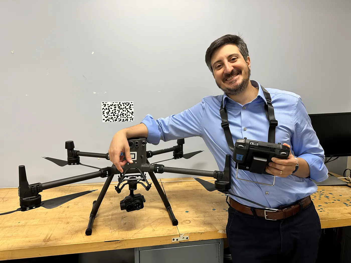 Mechanical Engineering Asst. Prof. Alessandro Sabato drapes his arm over a drone while wearing a remote control on his neck