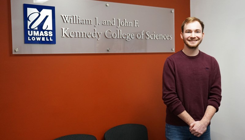 Sam Colby is standing next to the Kennedy of Science sign 