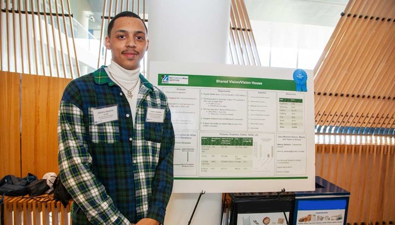 Sammy Santana poses in front a board describing his project to create an educational nonprofit called “Shared Vision/Vision House” at the UMass Lowell Difference Maker Idea Challenge.