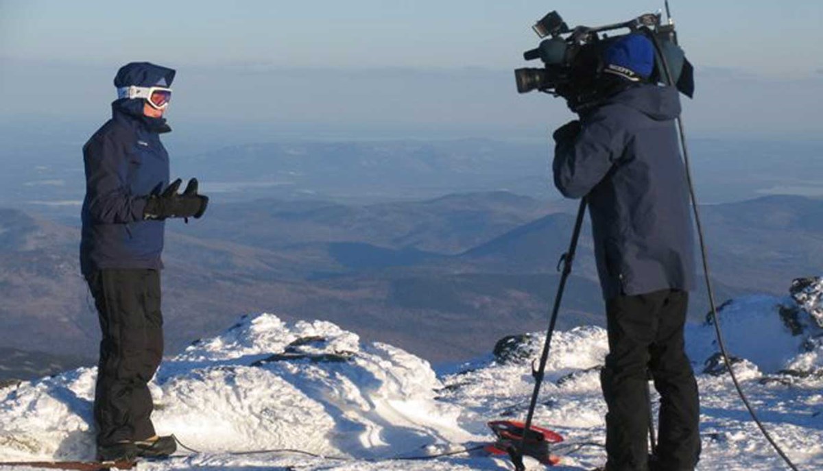 Sarah Long reports from Mount Washington as a person with a camera films her.