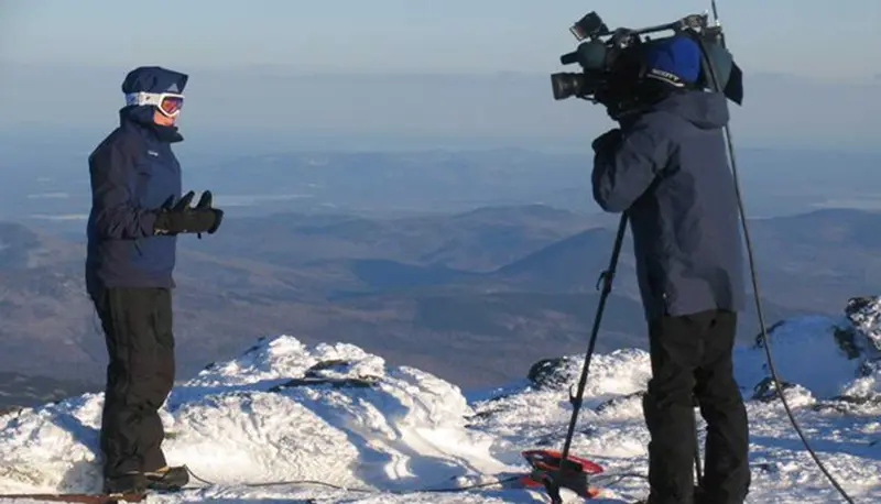 Sarah Long reports from Mount Washington as a person with a camera films her.